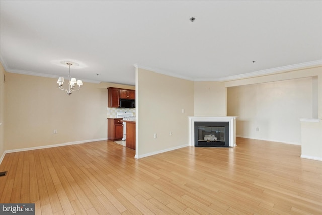 unfurnished living room with light wood-type flooring, a chandelier, crown molding, and a glass covered fireplace