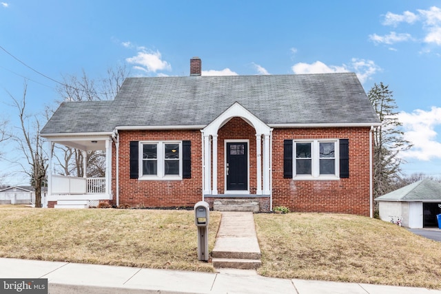 view of front of house featuring a porch, brick siding, roof with shingles, a chimney, and a front yard