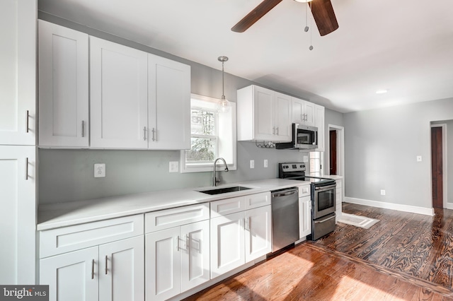 kitchen with dark wood-style flooring, stainless steel appliances, light countertops, white cabinetry, and a sink