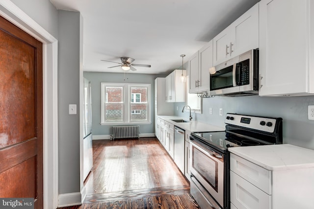 kitchen with radiator, wood finished floors, stainless steel appliances, white cabinetry, and a sink