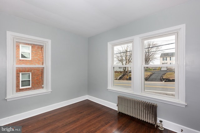 spare room featuring baseboards, dark wood-type flooring, and radiator