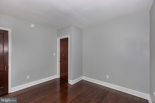 empty room featuring baseboards and dark wood-type flooring