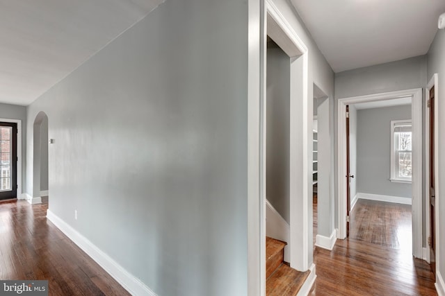 corridor featuring dark wood-style floors, baseboards, stairway, and arched walkways