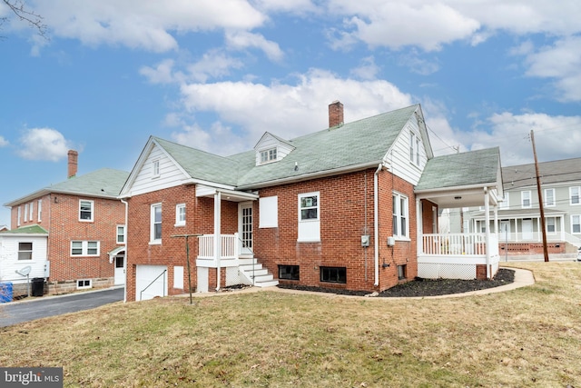 rear view of property with driveway, a chimney, a lawn, and brick siding