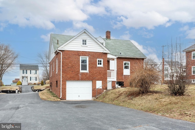 exterior space featuring aphalt driveway, brick siding, a chimney, and a garage