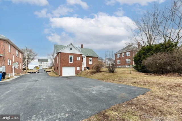 exterior space with an attached garage, brick siding, driveway, a residential view, and a chimney