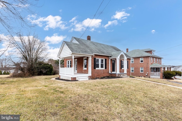 view of front of property with a chimney, brick siding, a front lawn, and a porch