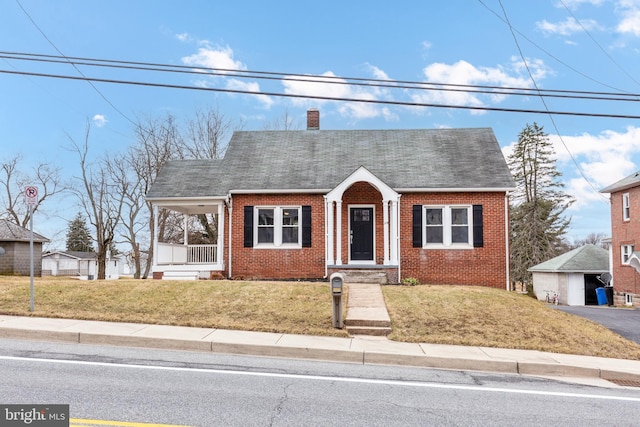 view of front of property with a chimney, roof with shingles, a front lawn, a porch, and brick siding