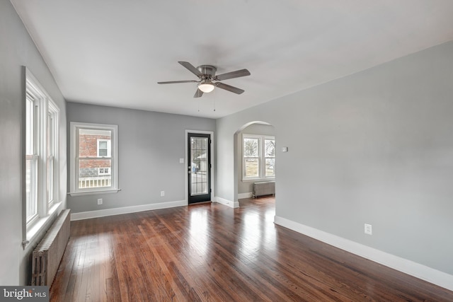 spare room with arched walkways, dark wood-style flooring, and radiator