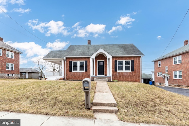 bungalow featuring brick siding, a chimney, a front yard, and a shingled roof