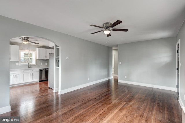 unfurnished living room featuring arched walkways, dark wood finished floors, a ceiling fan, a sink, and baseboards