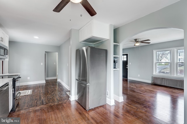 kitchen with white cabinets, dark wood finished floors, radiator, ceiling fan, and stainless steel appliances