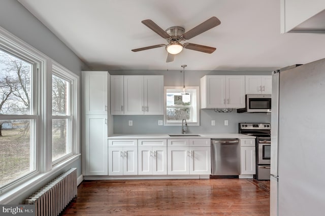 kitchen featuring stainless steel appliances, radiator heating unit, a sink, and white cabinetry