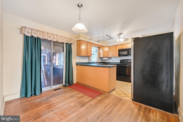 kitchen featuring light wood finished floors, visible vents, dark countertops, decorative light fixtures, and black appliances