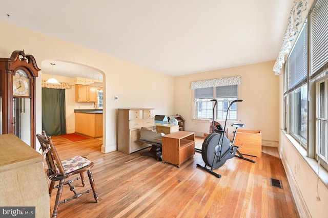 office with arched walkways, light wood-type flooring, visible vents, and baseboards