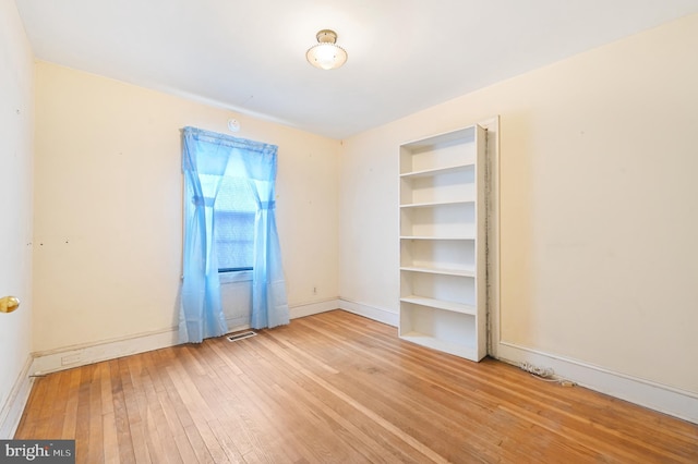 unfurnished room featuring light wood-style flooring, built in shelves, visible vents, and baseboards