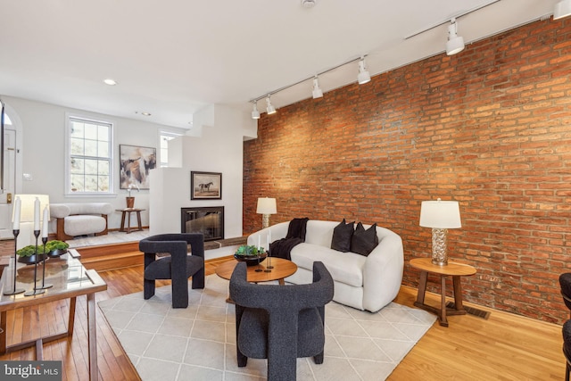 living room featuring a glass covered fireplace, light wood-style floors, and brick wall