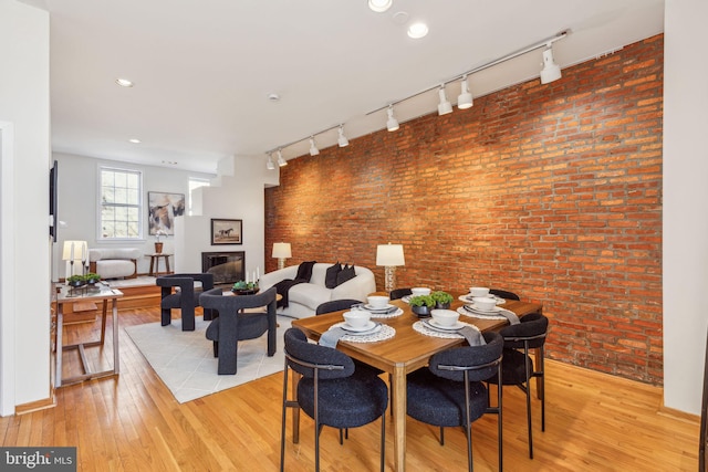 dining room featuring light wood finished floors, a glass covered fireplace, recessed lighting, and brick wall