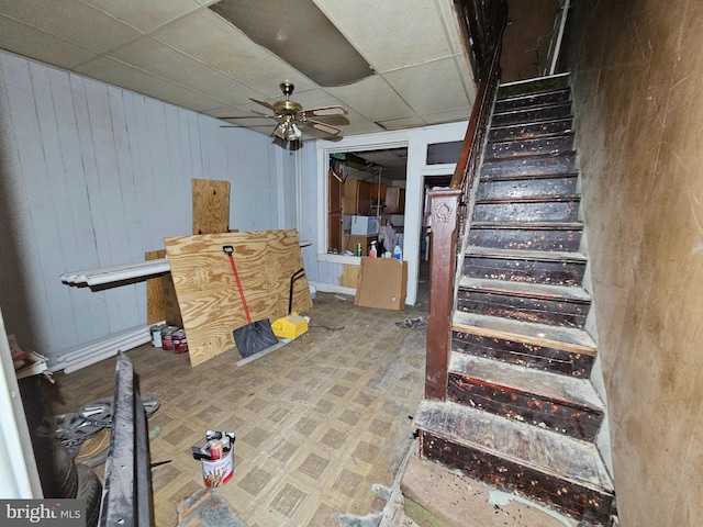 staircase featuring a paneled ceiling, wood walls, and a ceiling fan