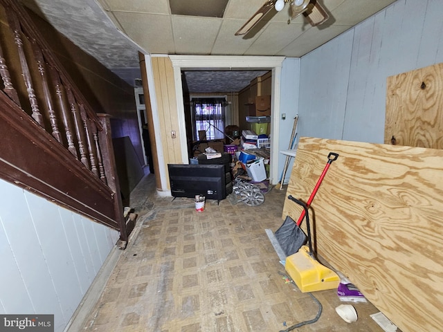 interior space with ceiling fan, wooden walls, a drop ceiling, and tile patterned floors