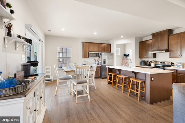 kitchen with a center island with sink, light wood finished floors, a breakfast bar area, stainless steel appliances, and light countertops