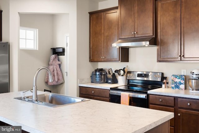 kitchen featuring light countertops, a kitchen island with sink, a sink, stainless steel range with electric stovetop, and under cabinet range hood