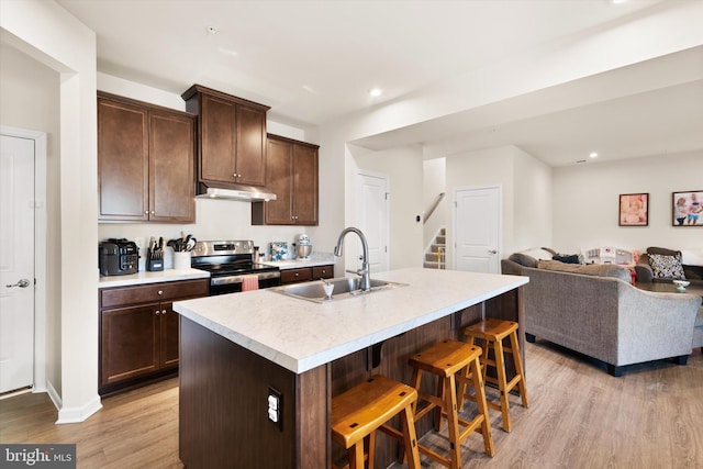 kitchen featuring light countertops, a kitchen island with sink, stainless steel range with electric cooktop, a sink, and under cabinet range hood