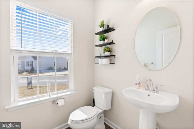 half bath with baseboards, plenty of natural light, and toilet