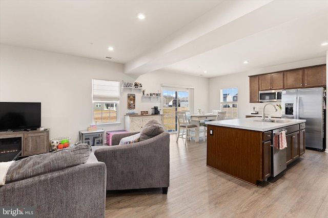 kitchen featuring stainless steel appliances, a center island with sink, open floor plan, and light countertops