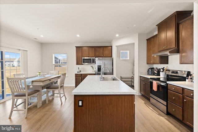 kitchen with appliances with stainless steel finishes, a kitchen island with sink, light countertops, under cabinet range hood, and a sink