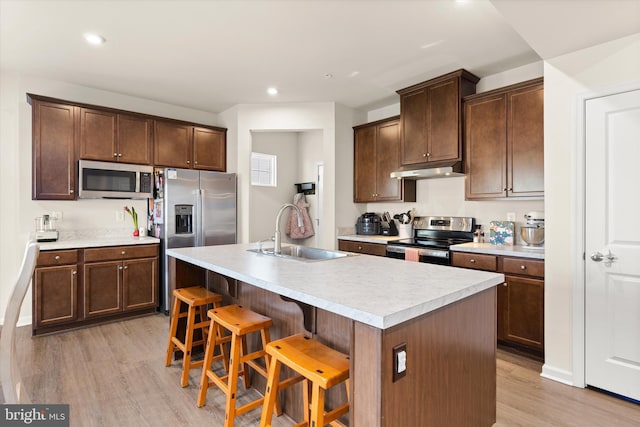 kitchen featuring a center island with sink, light countertops, appliances with stainless steel finishes, under cabinet range hood, and a kitchen bar