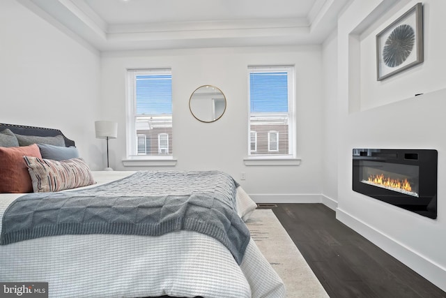 bedroom with a glass covered fireplace, dark wood-style flooring, a raised ceiling, and baseboards