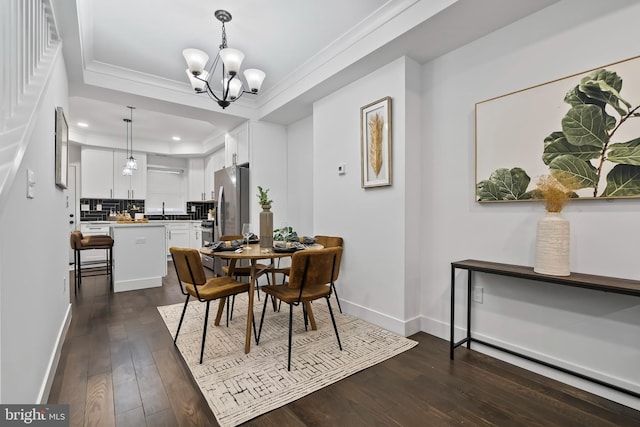 dining space featuring a notable chandelier, dark wood-type flooring, baseboards, a tray ceiling, and crown molding