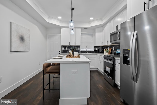 kitchen featuring stainless steel appliances, hanging light fixtures, white cabinets, and a center island