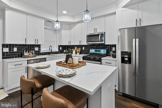 kitchen with hanging light fixtures, appliances with stainless steel finishes, white cabinets, and a center island