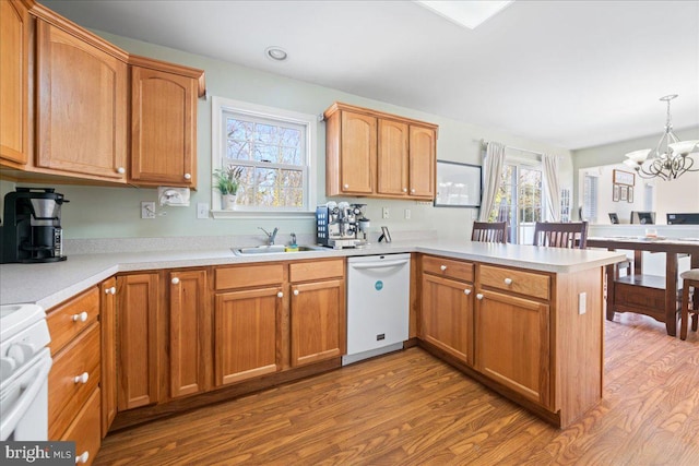 kitchen featuring decorative light fixtures, light countertops, a sink, white appliances, and a peninsula