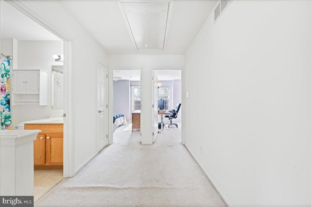 corridor with light carpet, attic access, visible vents, baseboards, and a sink