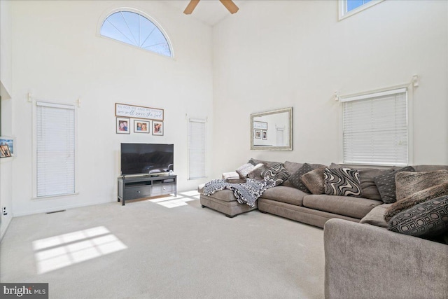 carpeted living room featuring ceiling fan, a high ceiling, and visible vents