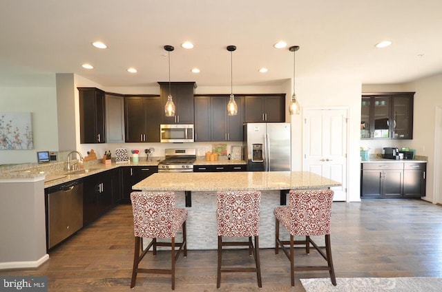 kitchen featuring pendant lighting, stainless steel appliances, a sink, a peninsula, and a kitchen bar