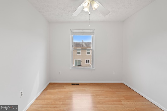 spare room featuring light wood finished floors, baseboards, visible vents, and a textured ceiling