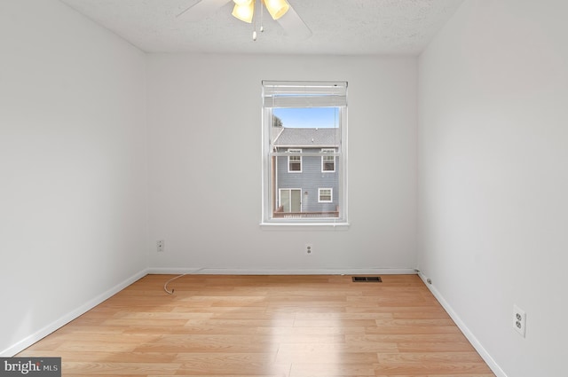 empty room with a textured ceiling, ceiling fan, visible vents, baseboards, and light wood finished floors