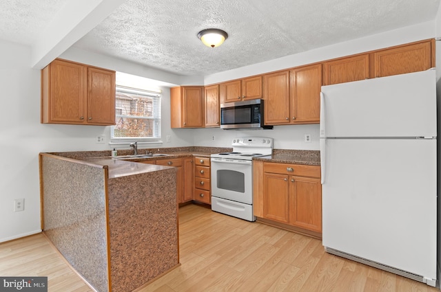 kitchen featuring white appliances, brown cabinetry, dark countertops, light wood-style floors, and a sink