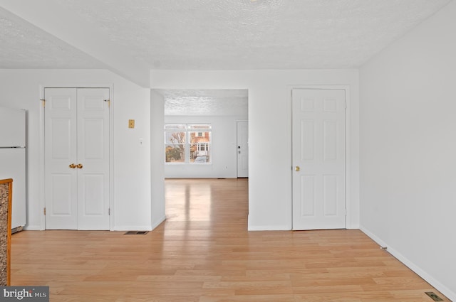 unfurnished room featuring light wood-style floors, visible vents, a textured ceiling, and baseboards