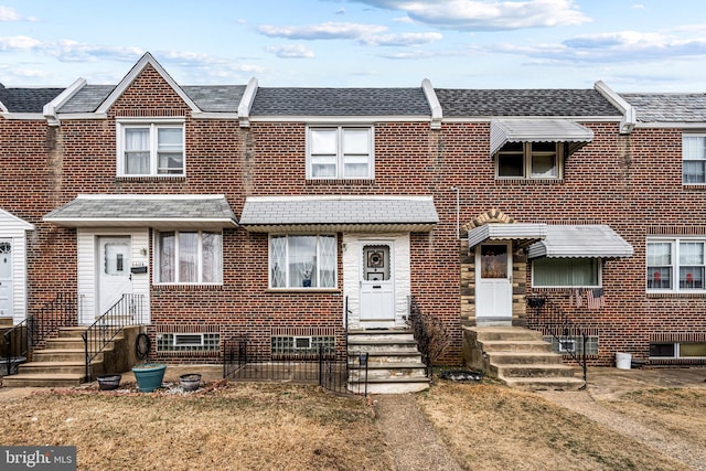 multi unit property with a shingled roof, entry steps, brick siding, and a front lawn