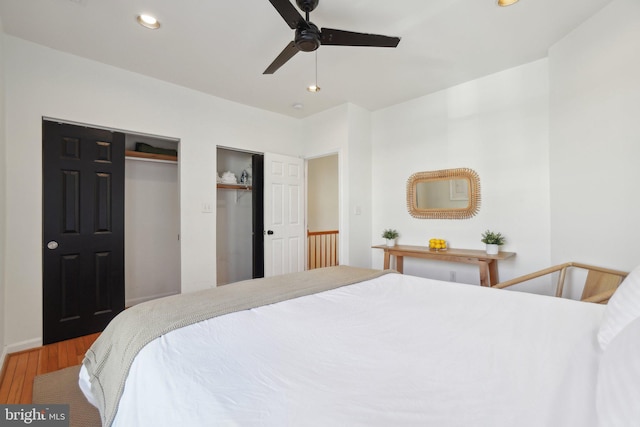 bedroom with recessed lighting, a ceiling fan, two closets, and wood finished floors