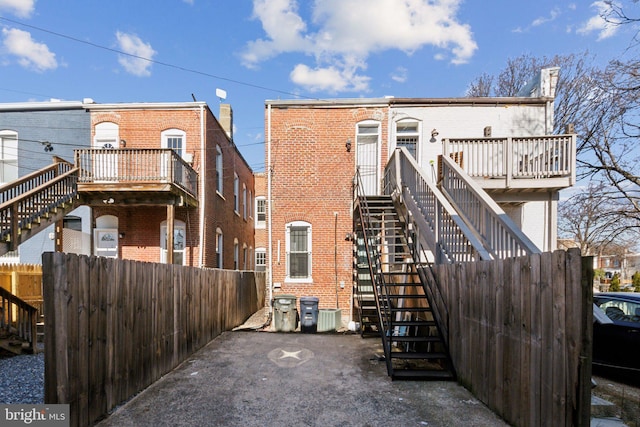 rear view of property featuring central AC, brick siding, stairway, and fence