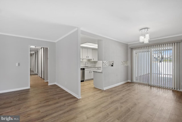 unfurnished living room with baseboards, a chandelier, light wood-type flooring, ornamental molding, and a sink