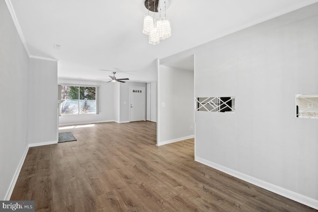 interior space featuring ceiling fan with notable chandelier, crown molding, baseboards, and wood finished floors