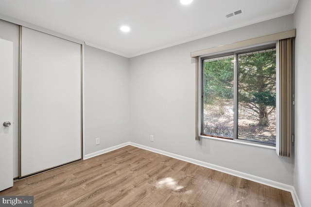 unfurnished bedroom featuring visible vents, wood finished floors, a closet, crown molding, and baseboards