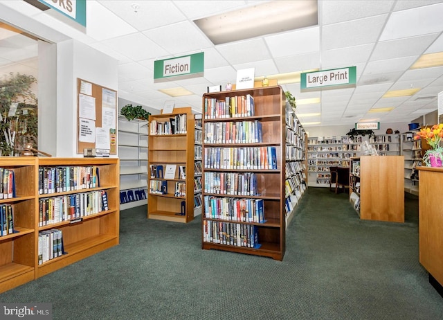 miscellaneous room featuring a drop ceiling, wall of books, and carpet floors